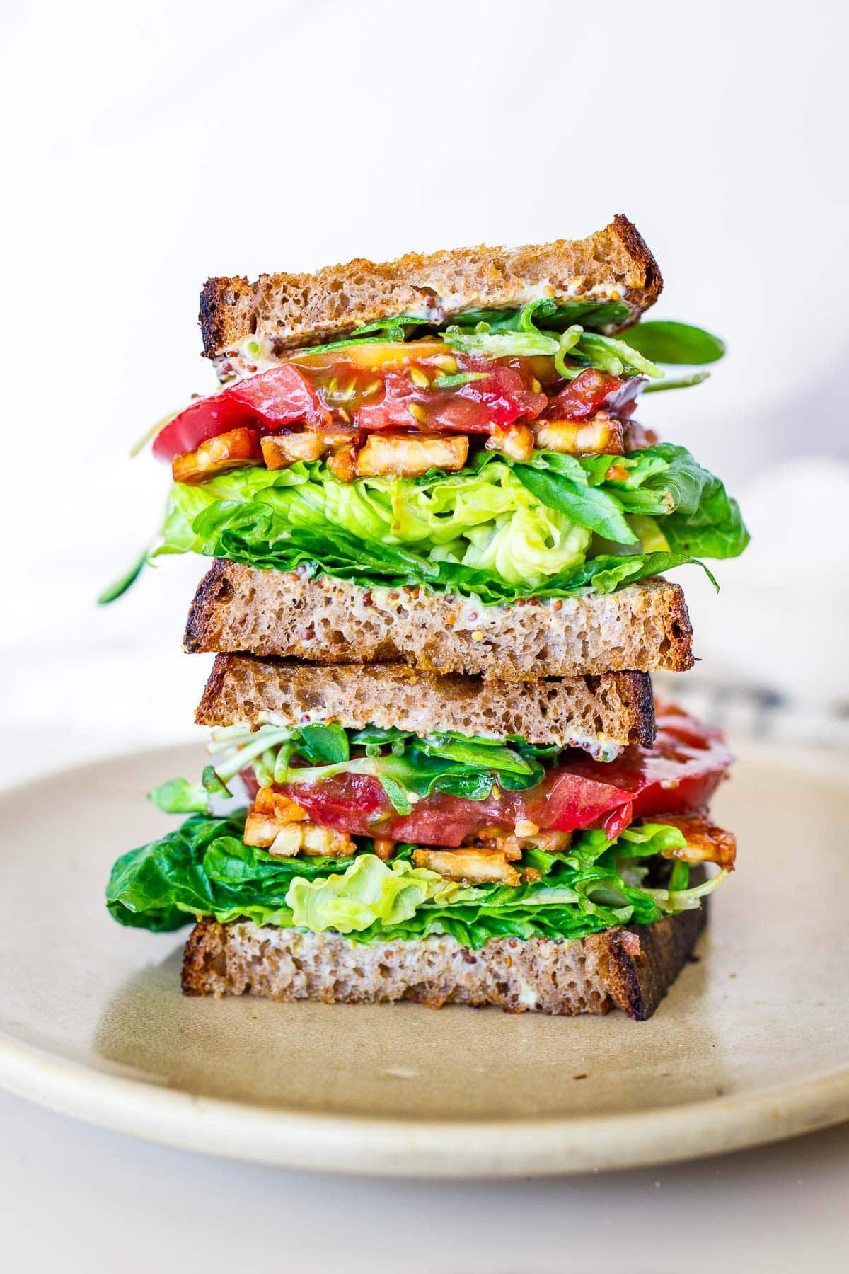 two vegan BLT sandwiches stacked atop one another with crisp lettuce, juicy tomato, and tempeh. 