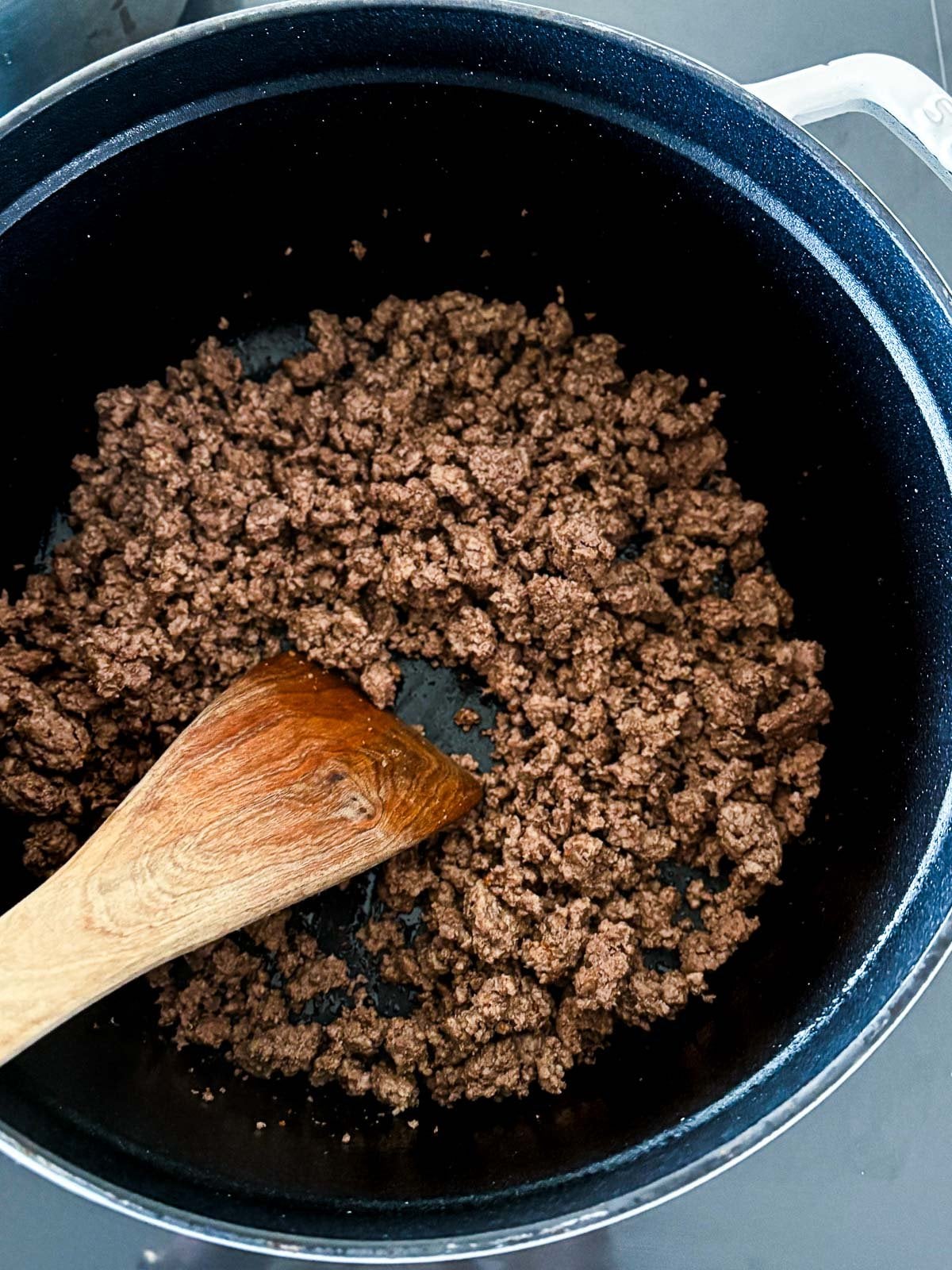 wood spatula stirring browning ground beef in large pot.