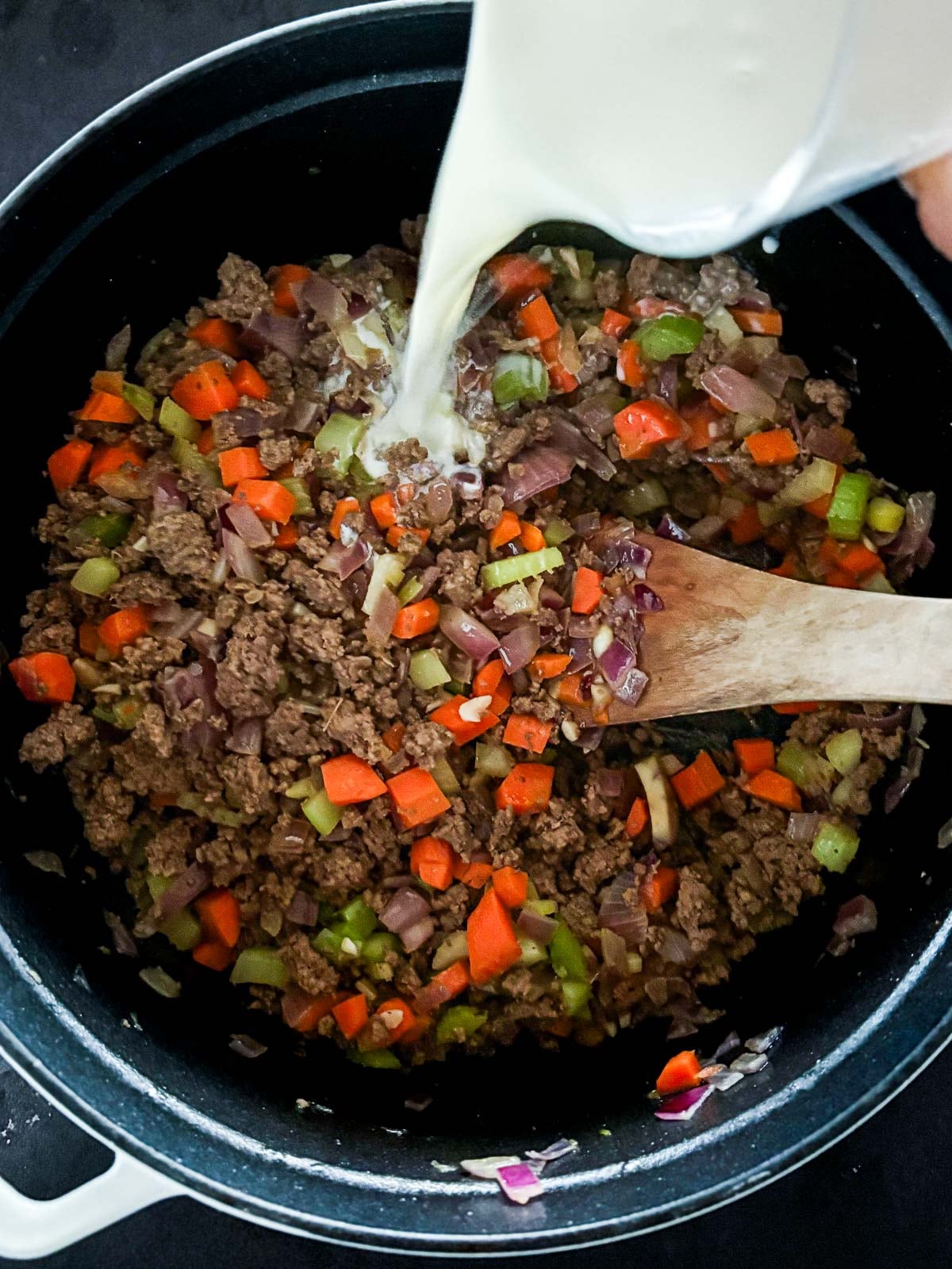 pouring milk into large pot of ground beef and diced veggies.