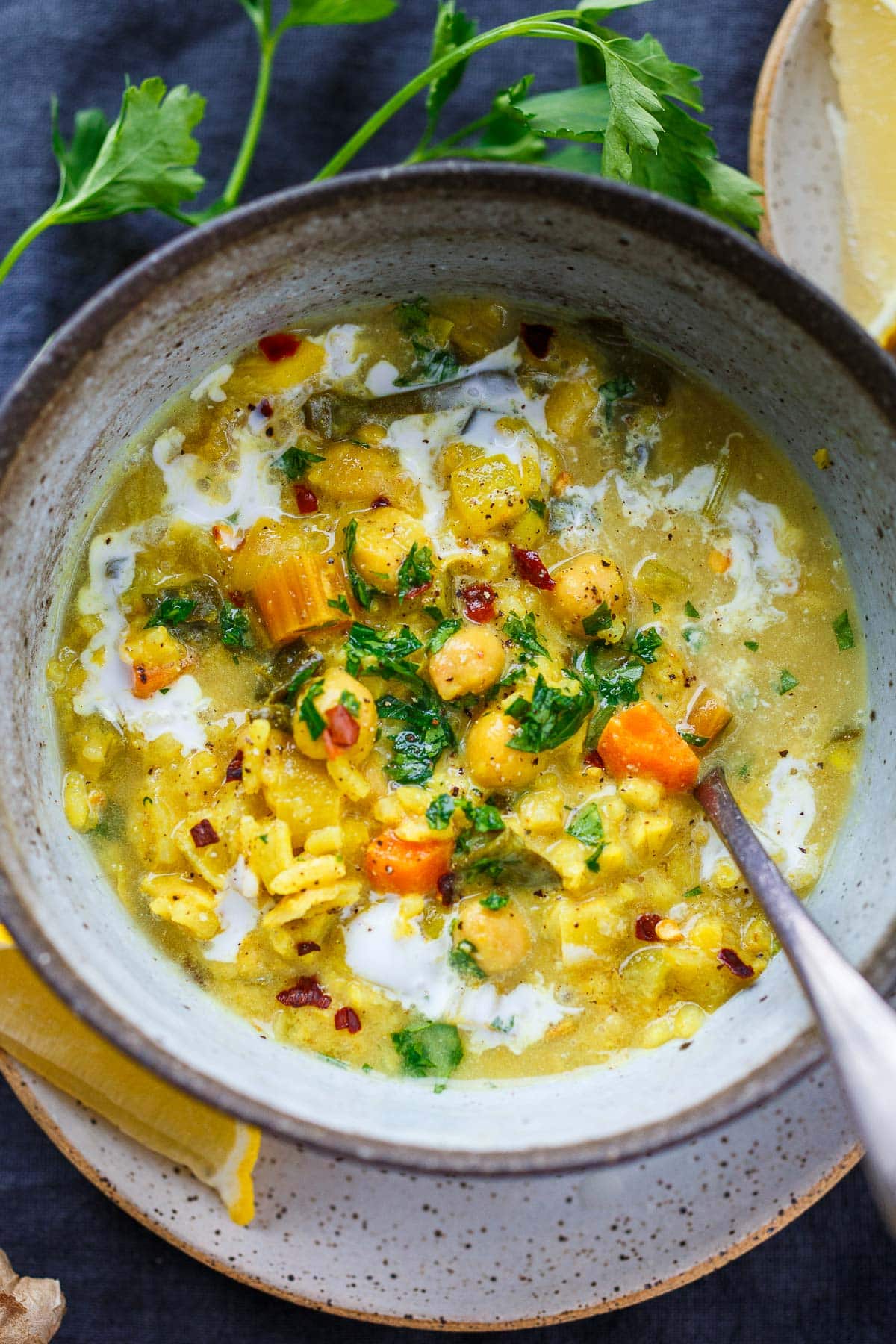 bowl of golden chickpea soup with veggies, rice, chickpeas, and a swirl of coconut, topped with fresh herbs and chili flakes. 