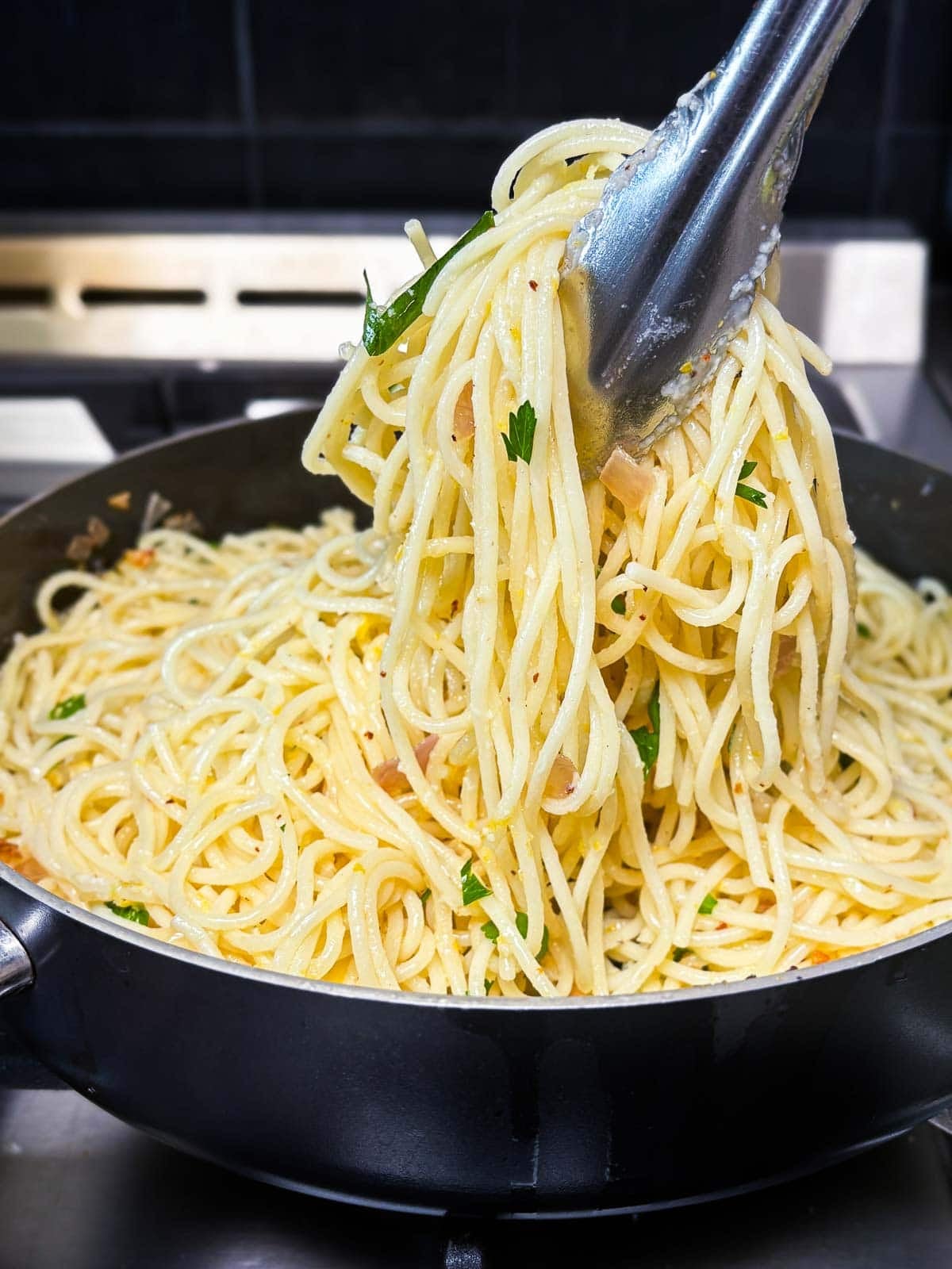 using tongs to pick up the lemon pasta from the pan. 
