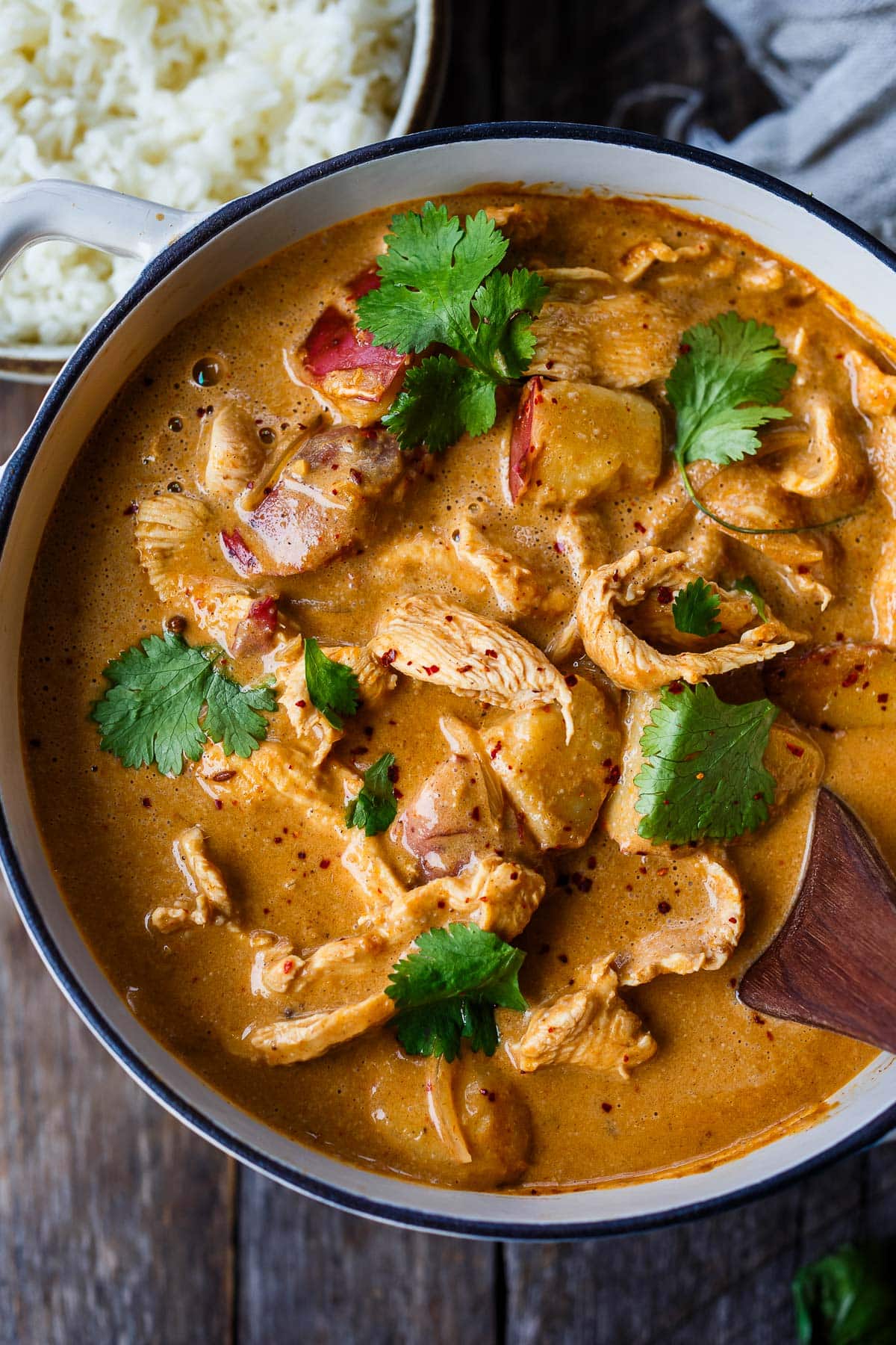 large pot with thai massaman curry with chicken and potatoes, topped with chili flakes and cilantro.