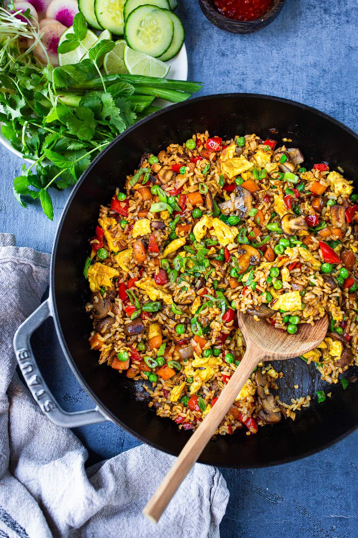 Nasi Goreng in a cast iron skillet with a wood spoon lifting up some of the Indonesian fried rice.