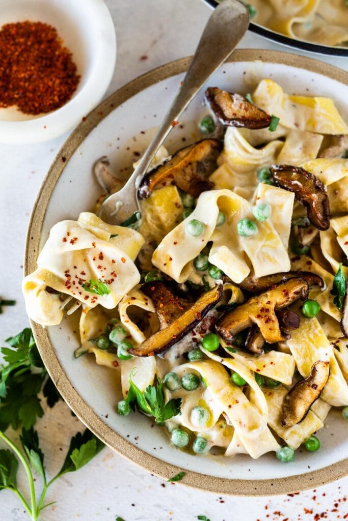 bowl of fettuccine with vegan alredo sauce, peas, mushrooms, and chili flakes. 