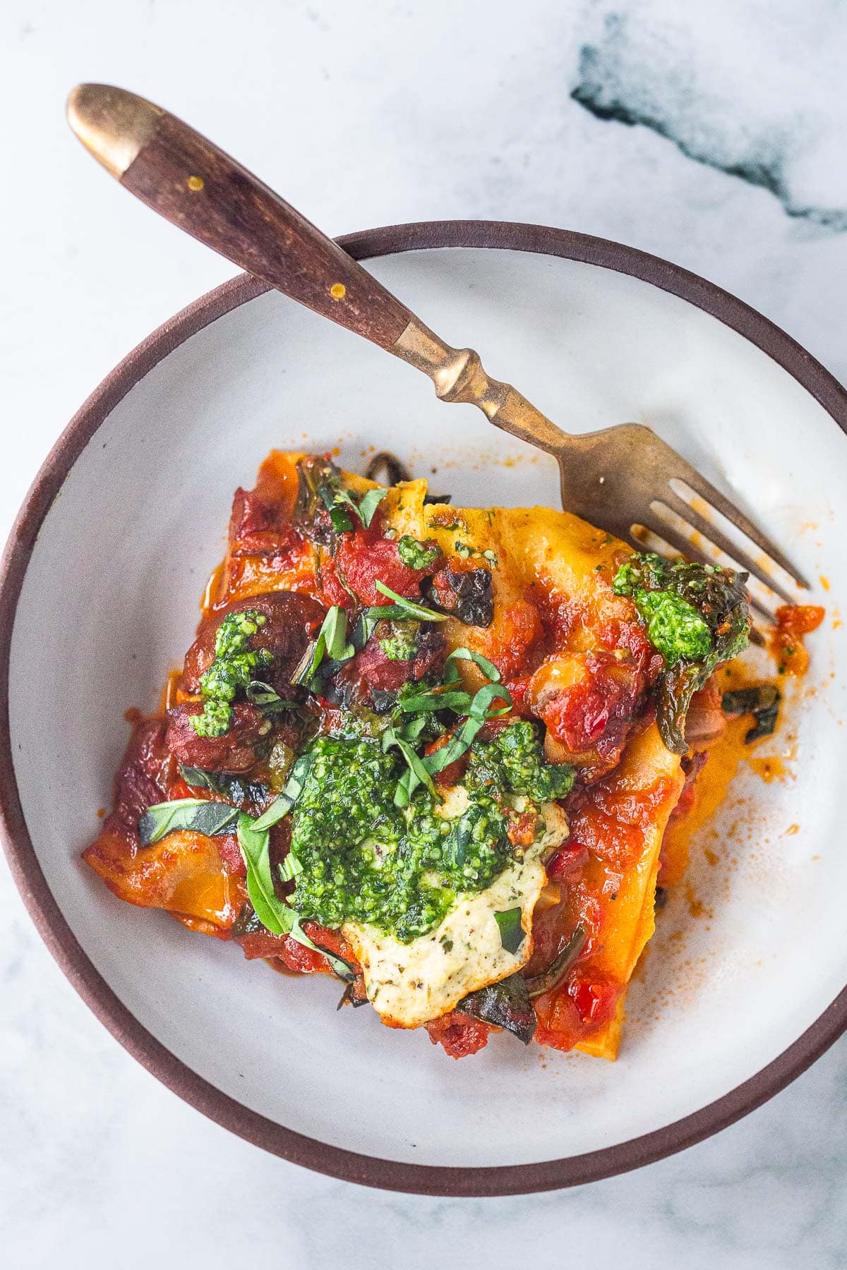 vegan lasagna on a plate with a fork, topped with pesto. 