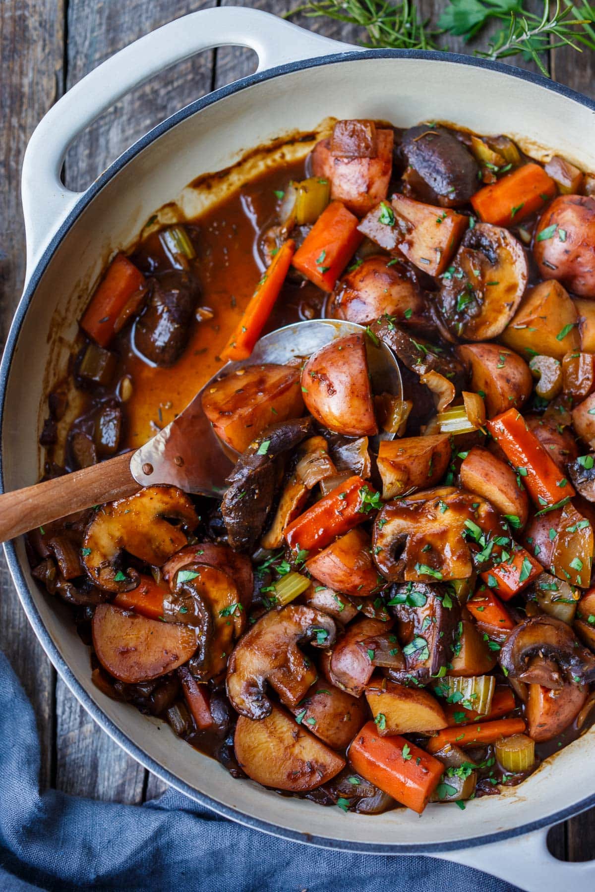 pot of vegetable stew with carrots, potatoes, mushrooms, celery, and onions with minced parsley and serving spoon. 