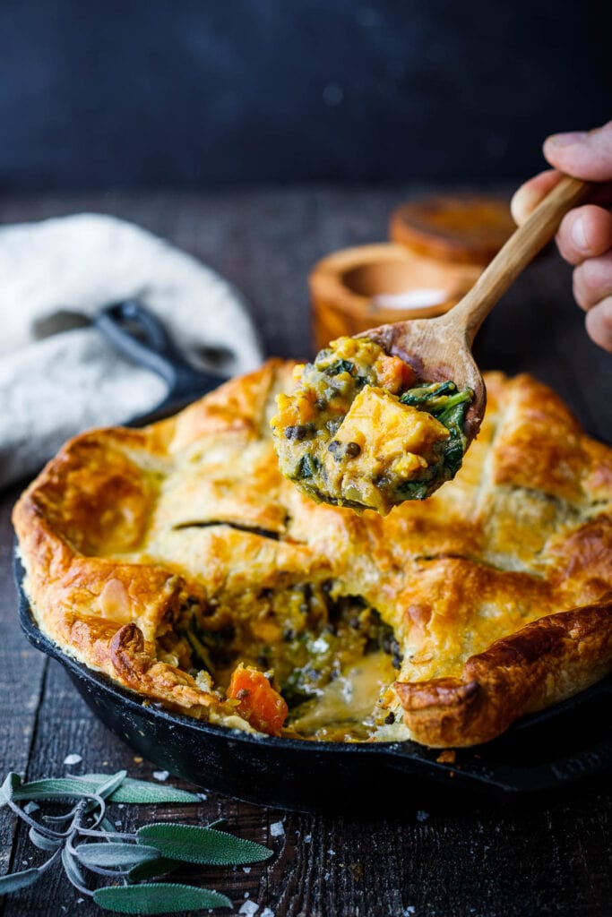 lentil pot pie with butternut squash with wood spoon lifted above the pie holding the delicious interior. 