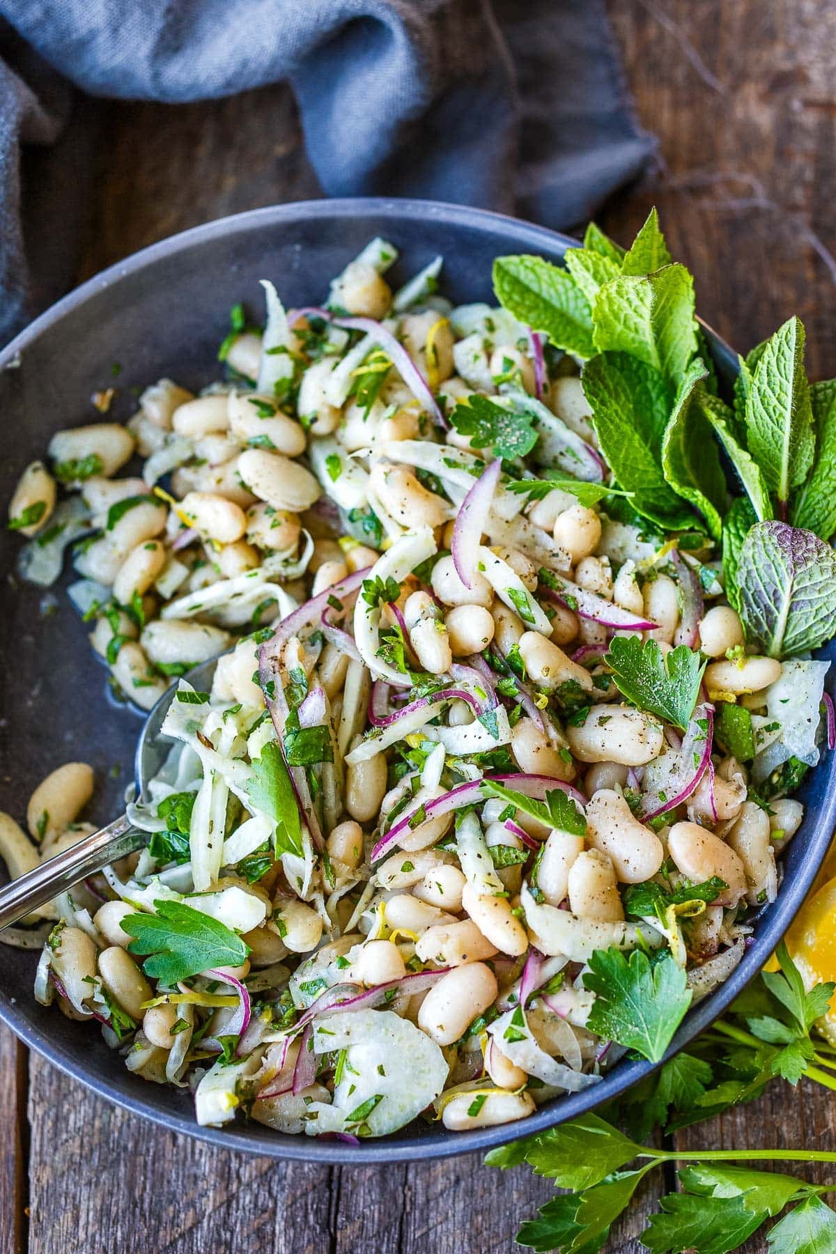 bowl of white bean salad with red onions and fresh herbs in bowl with silver spoon.